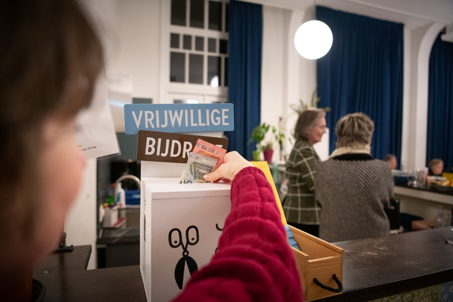 Iemand doet een bijdrage in de donatiepot van Repair Café Jeltje