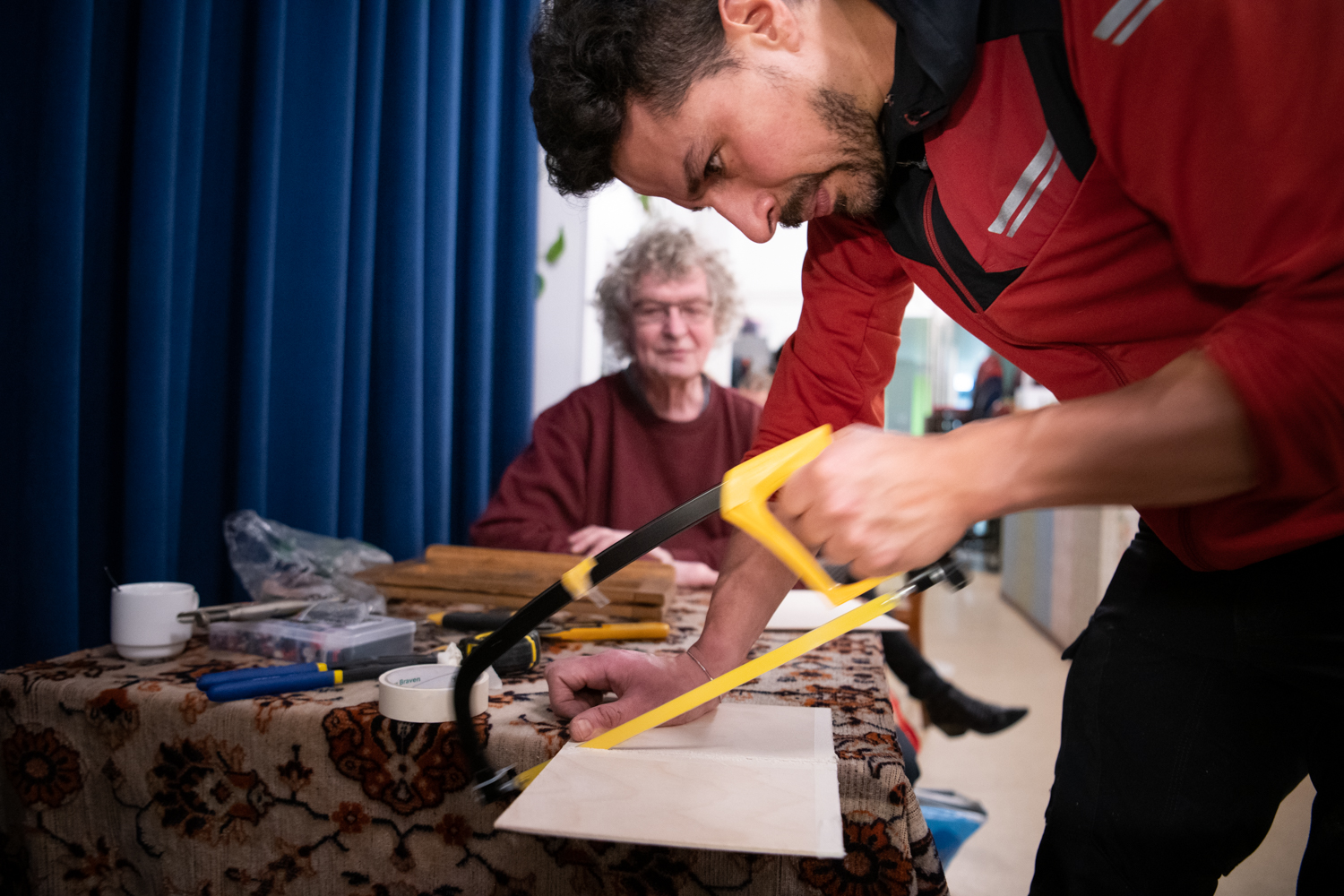 Jongeman repareert houten boekenstandaard voor bezoeker Repair Café Jeltje