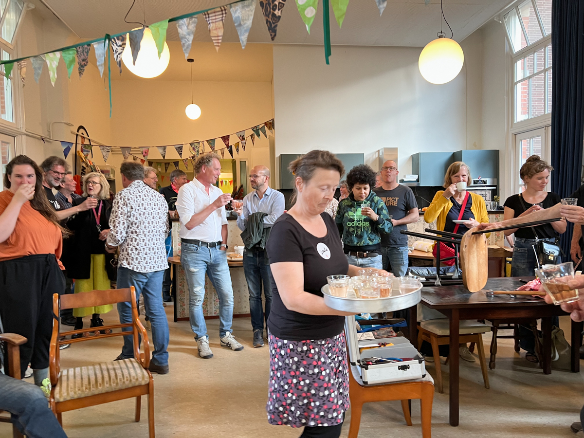 Gastvrouw deelt bubbels uit op het feest ter ere van vijf jaar Repair Café Jeltje